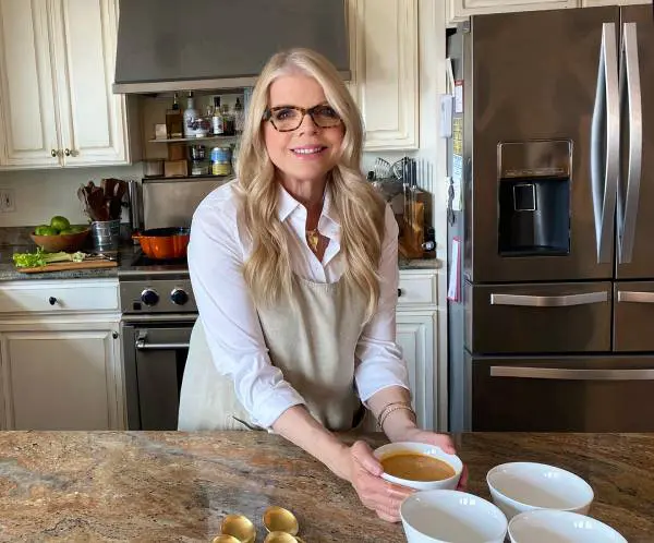 A woman in glasses and apron holding bowl of food.