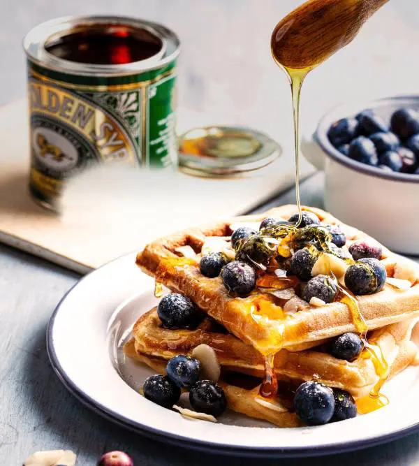 A plate of waffles with blueberries and syrup.